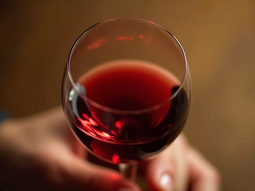 A hand elegantly holding a wine glass by the stem, demonstrating the proper swirling technique.